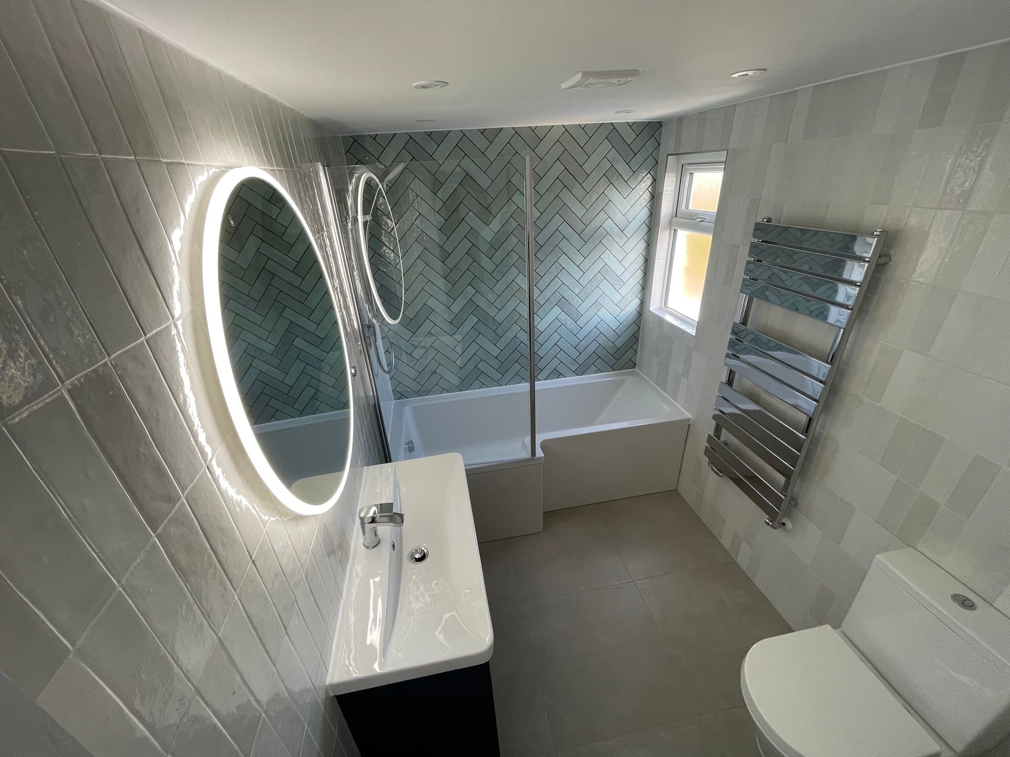 Premium bathroom with herringbone feature wall, LED mirror, and chrome heated towel rail — completed by ABC Tiling
