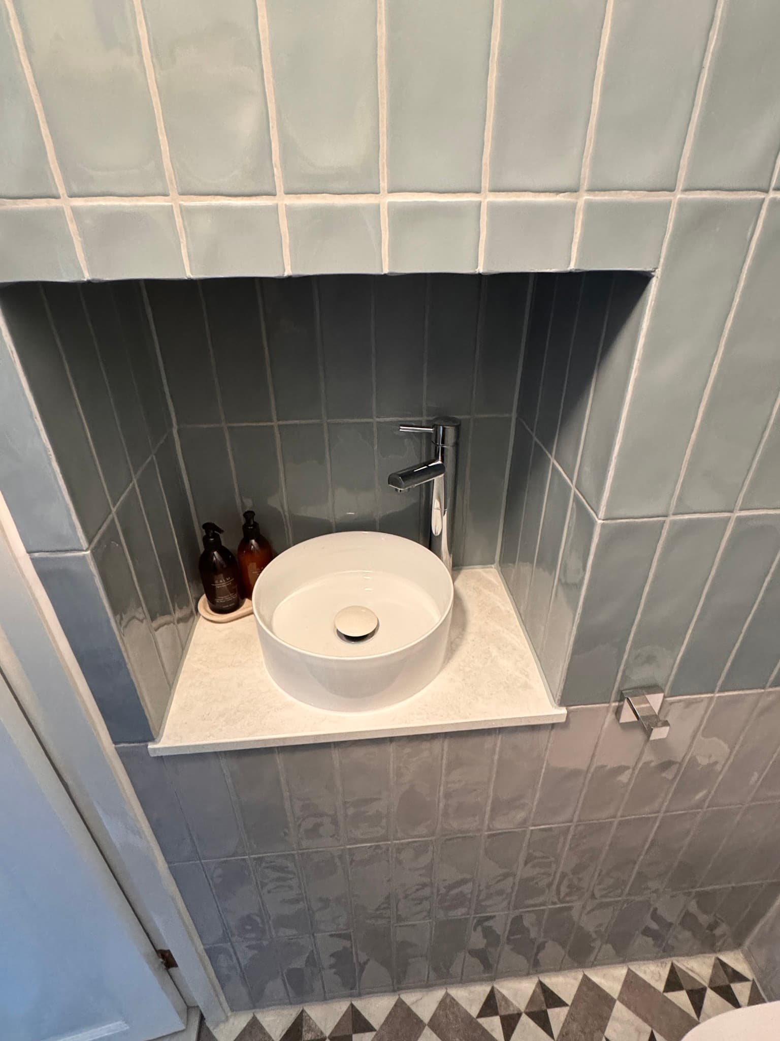 Basin niche detail with gloss grey subway tiles and geometric floor