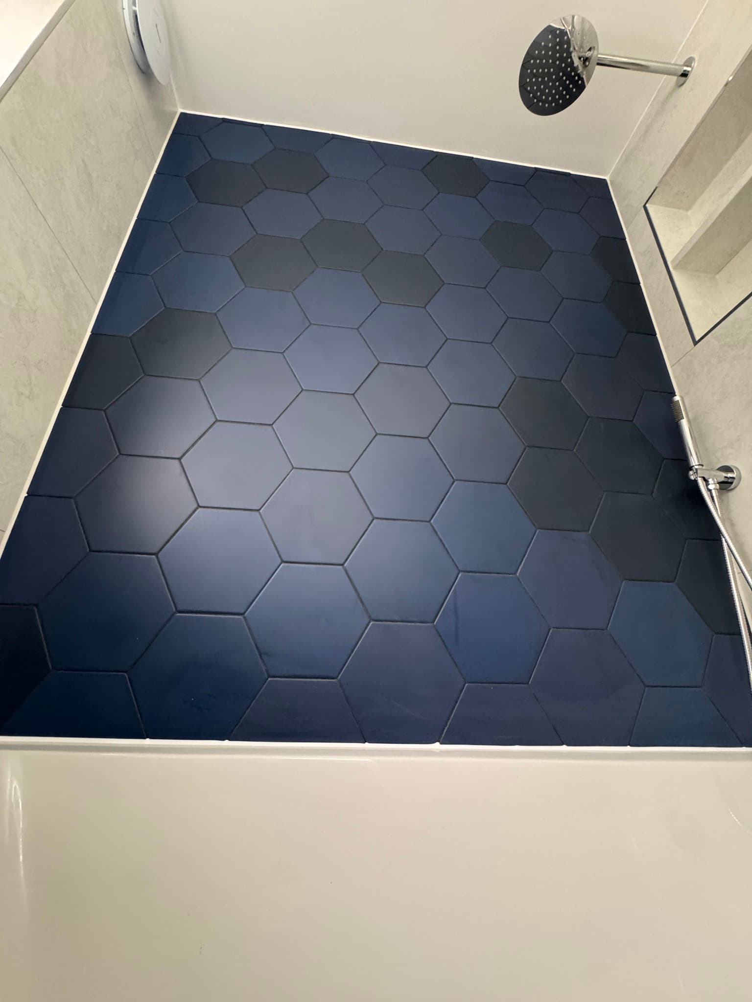 Walk-in shower floor with large format navy hexagonal tiles and chrome riser rail