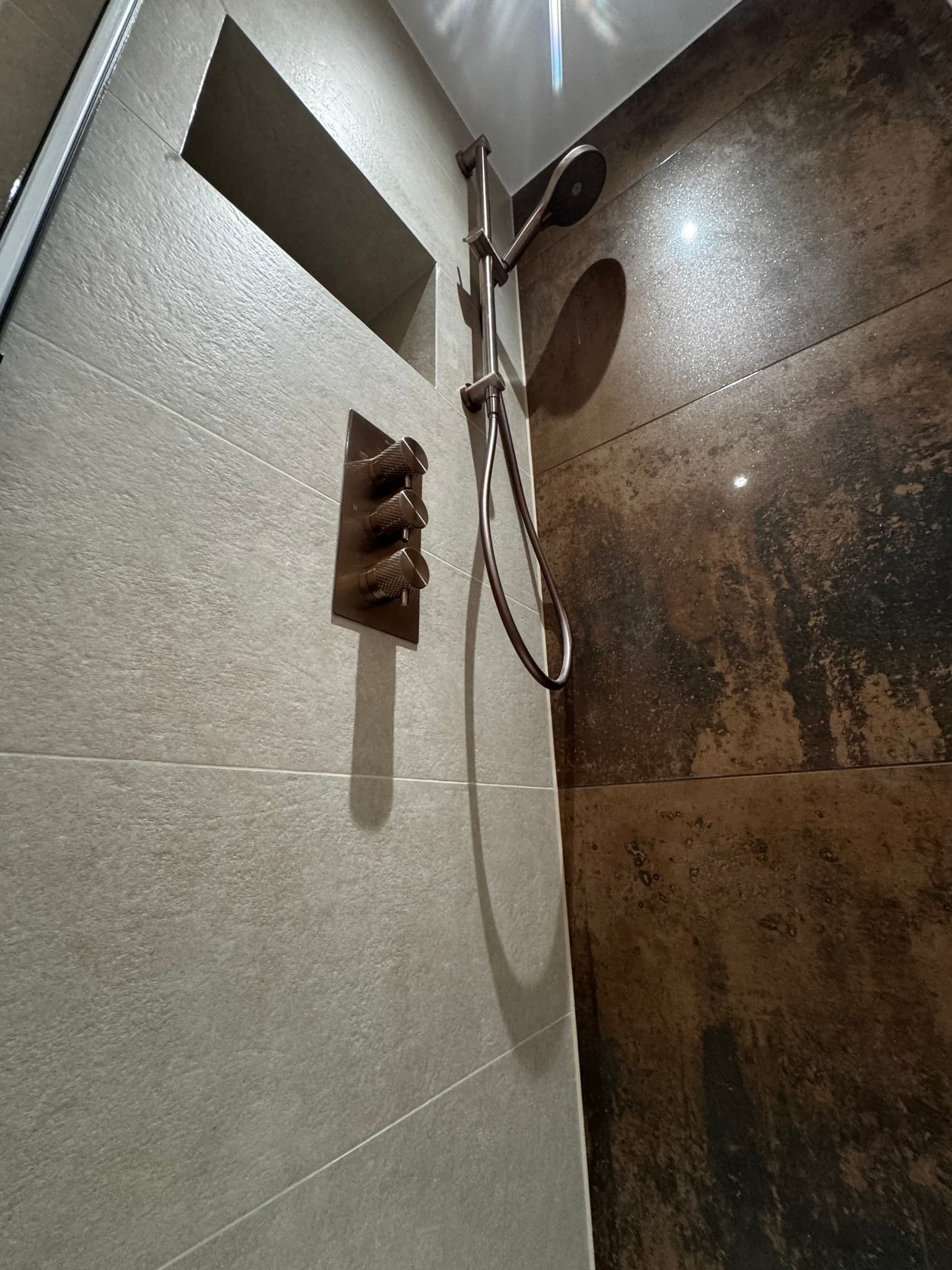 Shower enclosure with cream textured tiles contrasting with charcoal rust-effect feature tiles