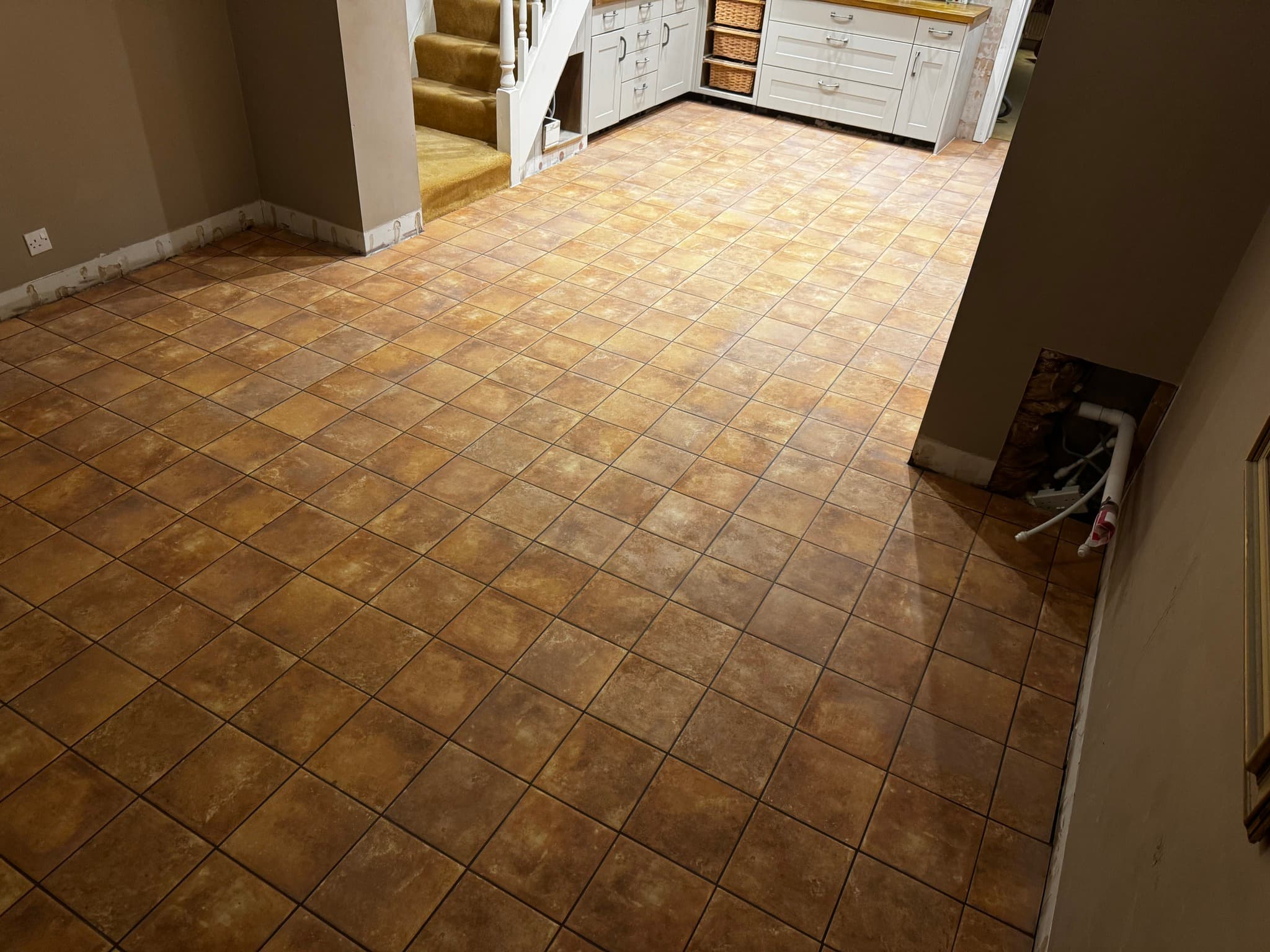 Open-plan kitchen-diner with warm terracotta travertine-effect floor tiles and white shaker units