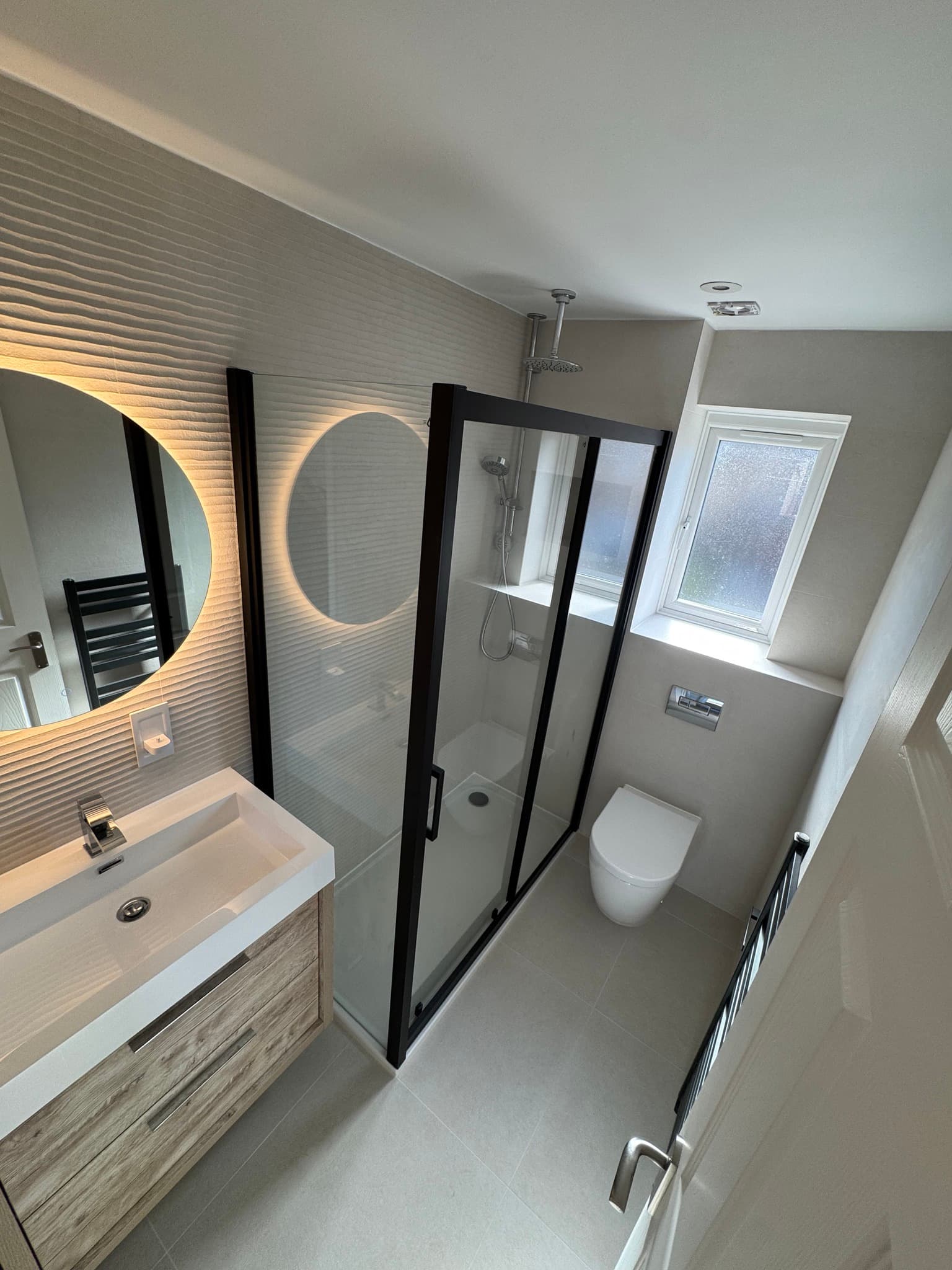 Modern bathroom with white wave-texture tiles and black-framed shower enclosure