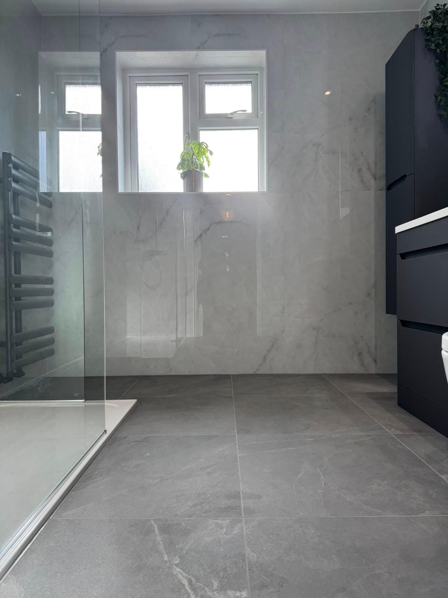 Spacious wet room with Calacatta marble-effect wall tiles, dark grey floor tiles, walk-in shower, black towel rail, and black vanity unit