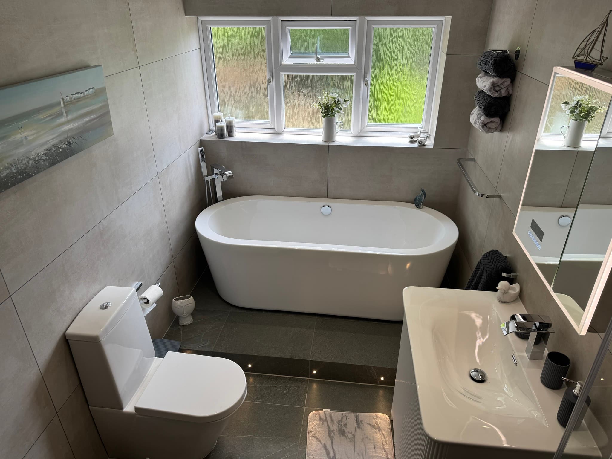 Family bathroom with grey stone-effect tiles, freestanding oval bath beneath triple window