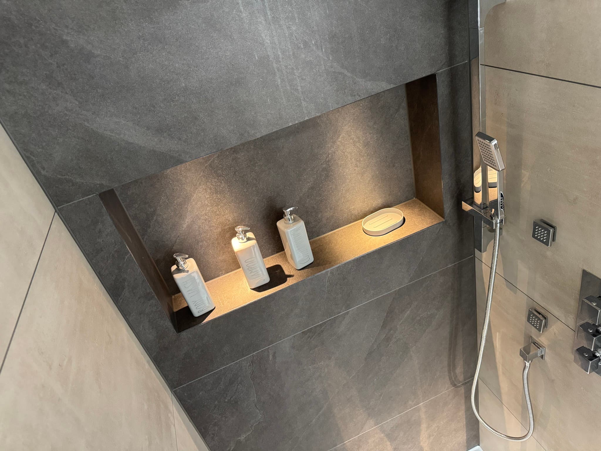 Illuminated recessed shower niche set into dark charcoal slate-effect tiled wall